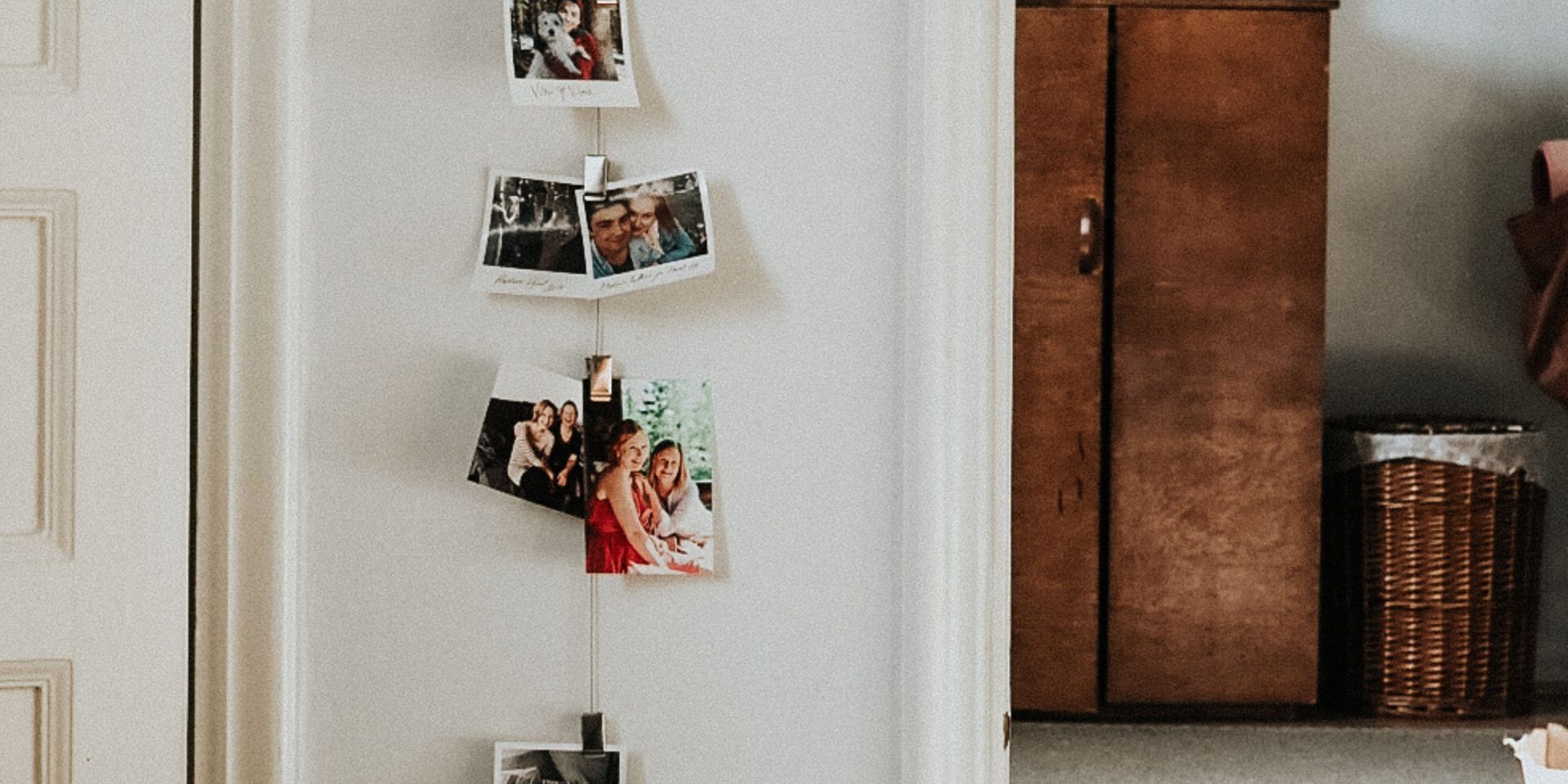 Kuvassa on etualalla seinällä polaroid-kuvia ripustettuna narusta roikkumaan ja taka-alalla taemmassa huoneessa ruskea vaatekaappi.